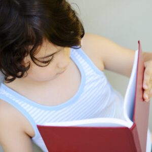 Child reading a red book, looking down.