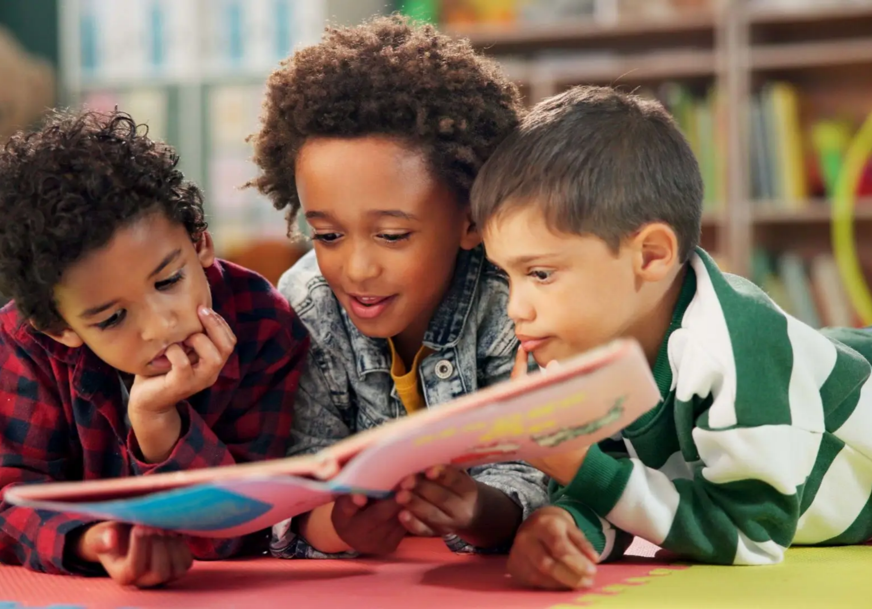 Children reading a book together on floor.