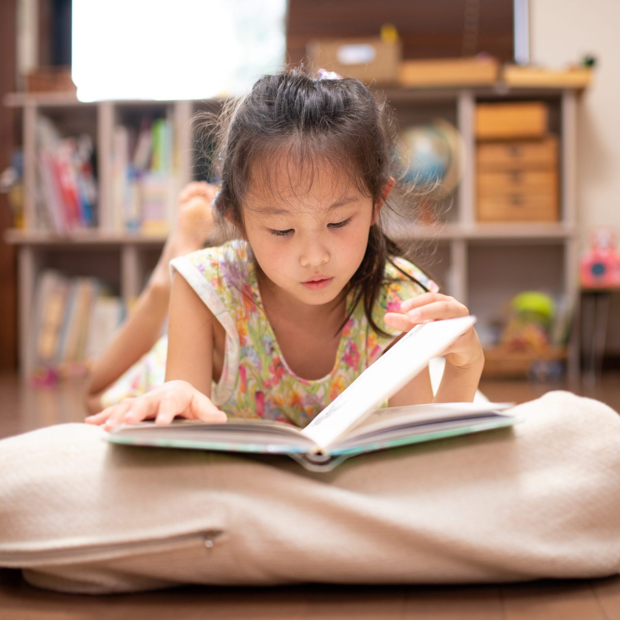 Girl reading book on floor cushion.