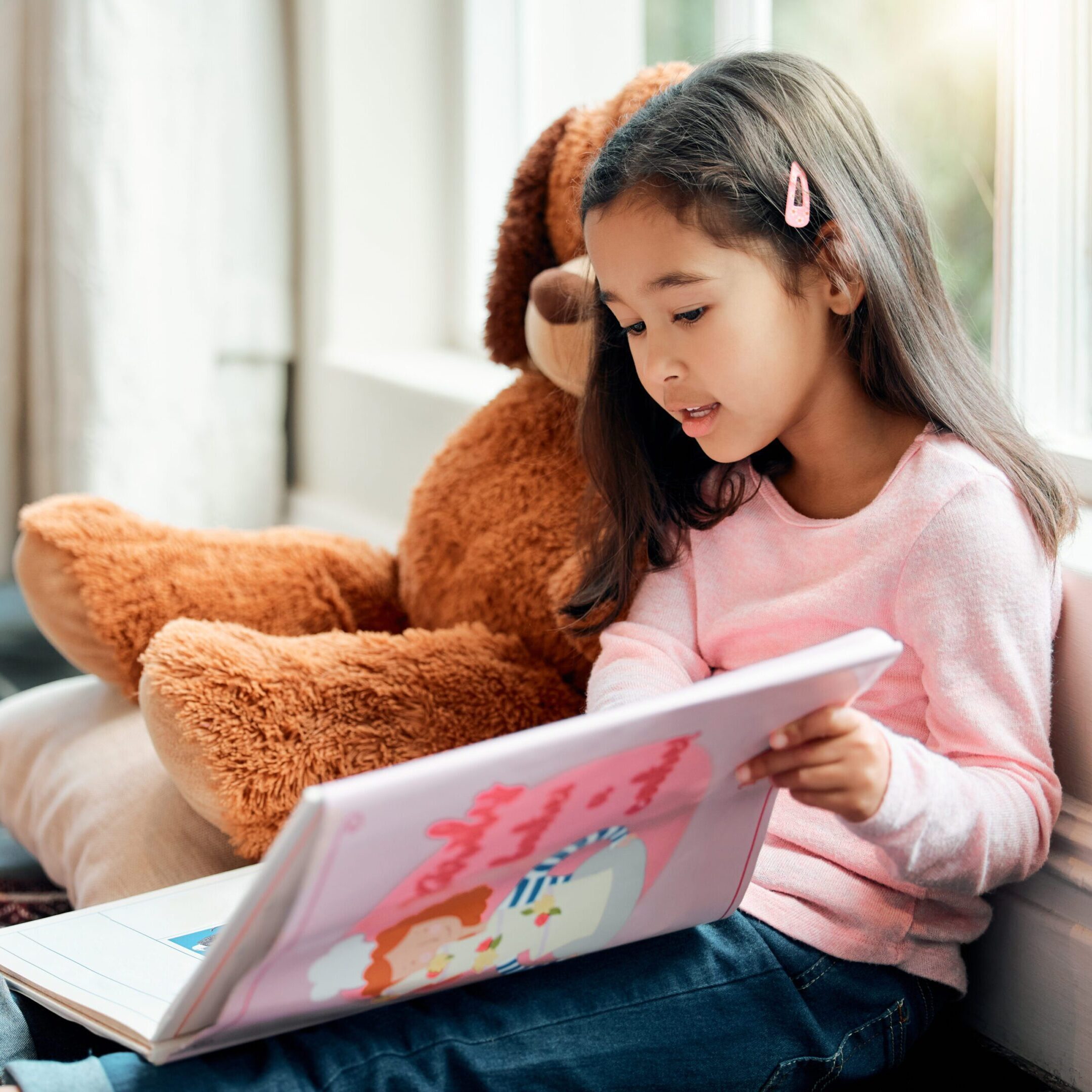 Girl reading book with stuffed bear.